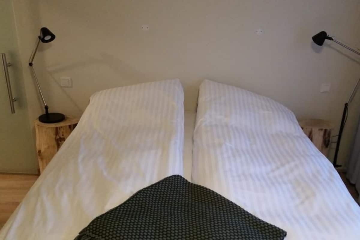 A bed with white linens, two bedside lamps, and a wooden nightstand.