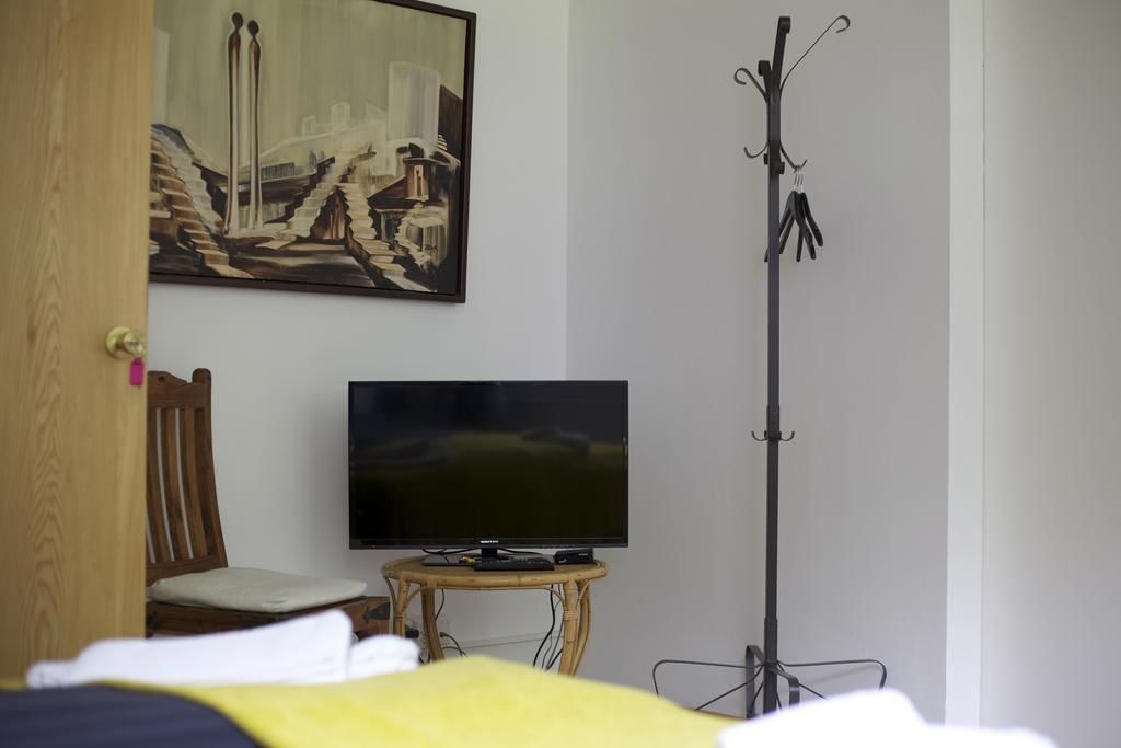 Une chambre d’hôtel avec un lit, un téléviseur posé sur une petite table, un porte-manteau et un tableau accroché au mur.