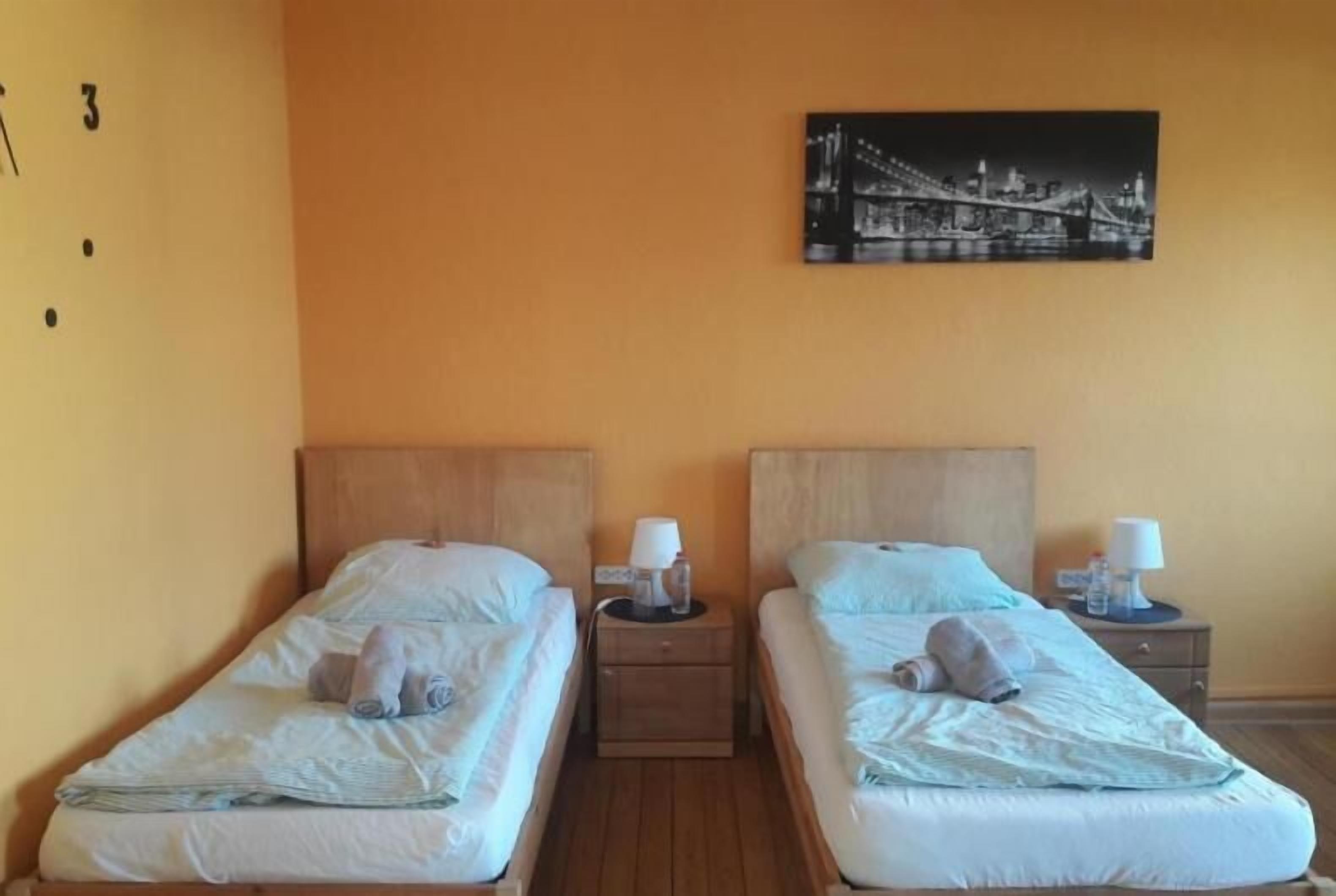 Une chambre d’hôtel avec deux lits simples, des têtes de lit en bois, des tables de chevet avec des lampes et un tableau encadré au mur.