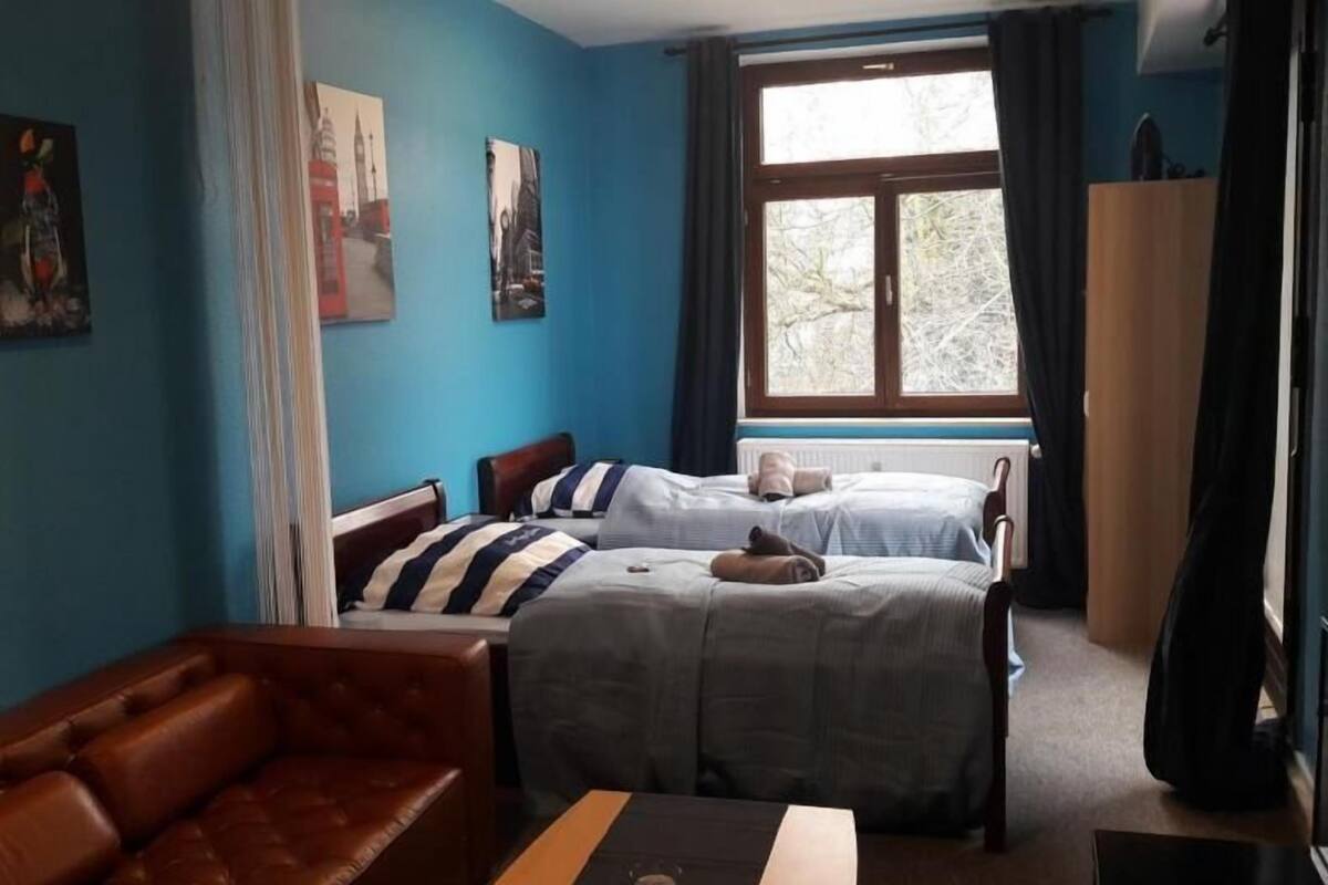 A room with two beds, a brown leather sofa, and a window with curtains.