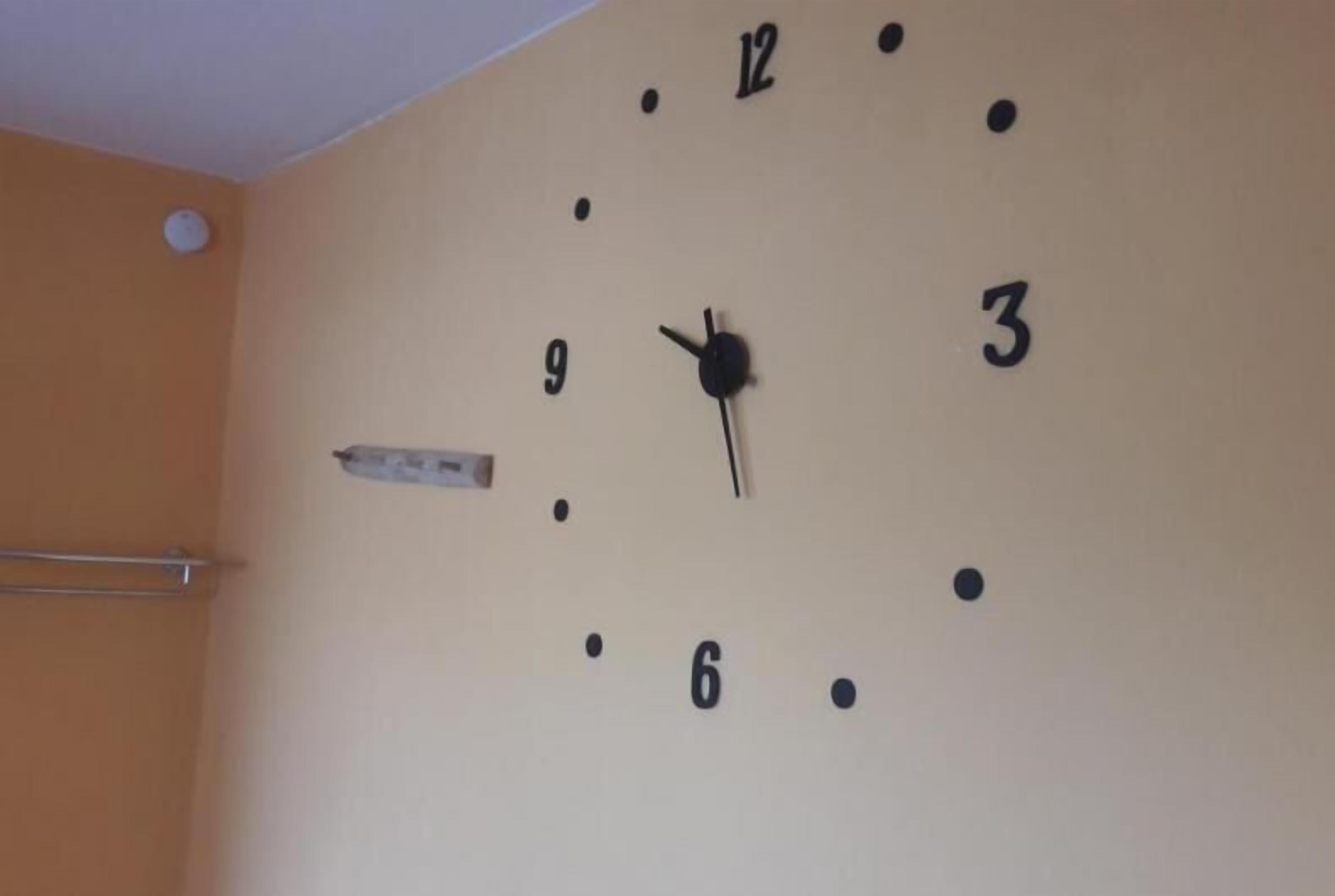 A wall clock with black hands and numbers, mounted on a beige wall.