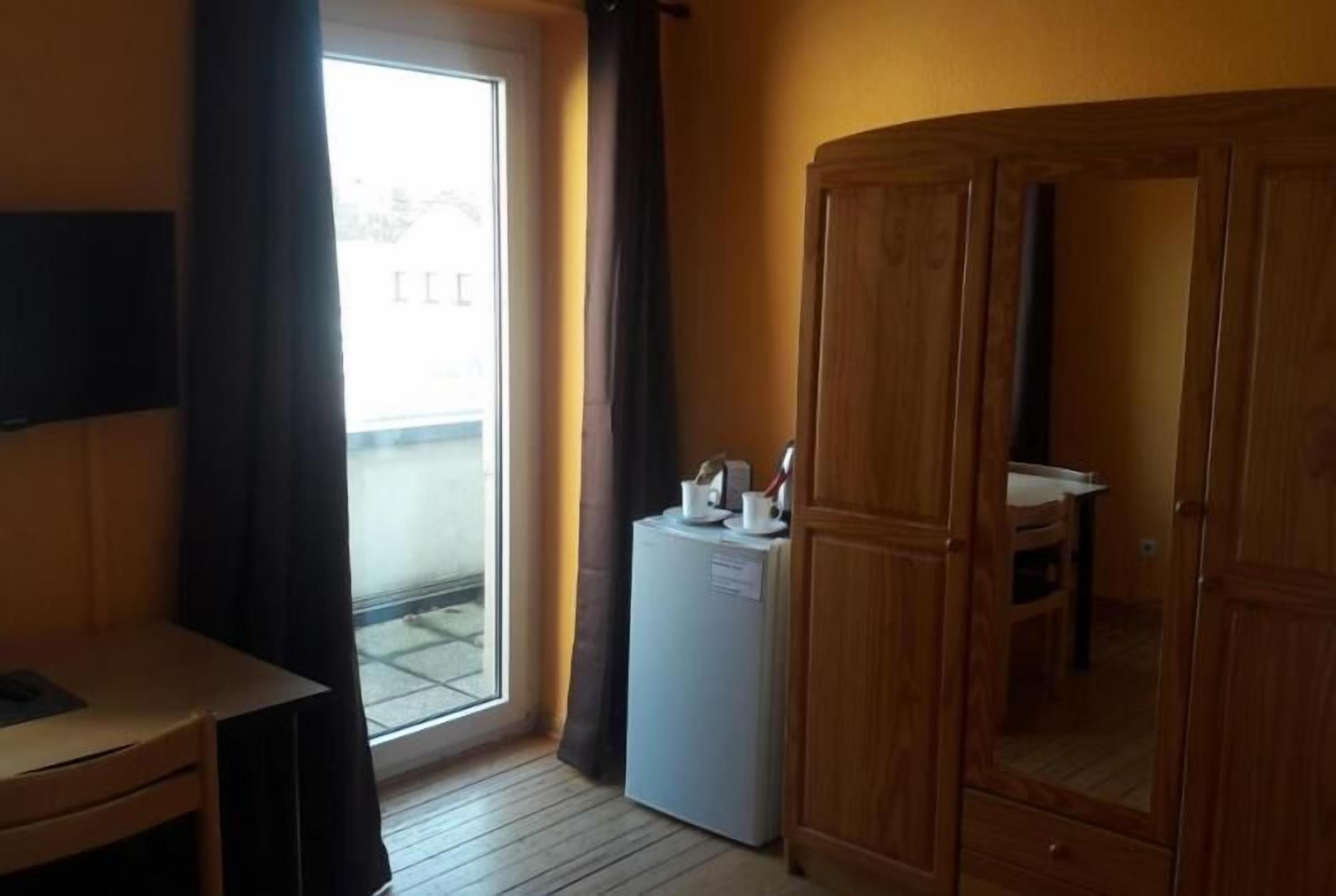 Une petite pièce comprenant un meuble en bois, un petit réfrigérateur, une table avec une chaise et une fenêtre avec des rideaux.