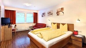 A modern hotel room with a wooden bed, red armchair, and a desk with a television.