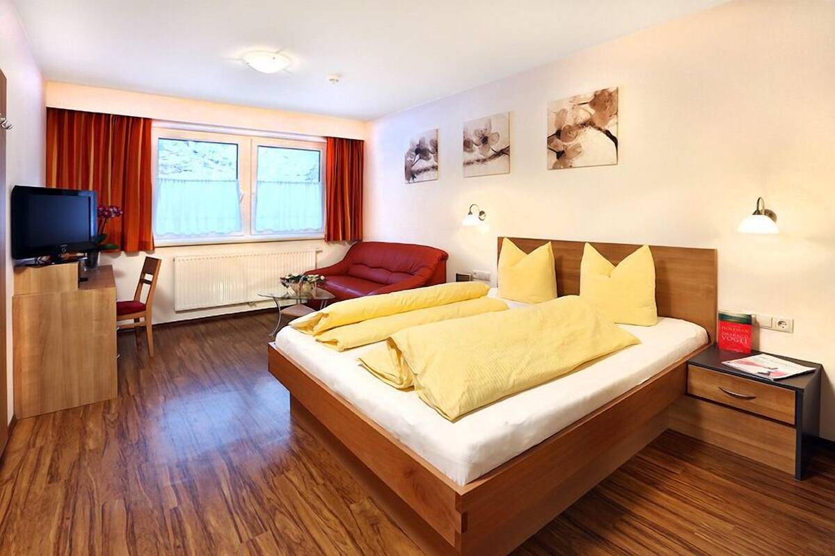 A modern hotel room with a wooden bed, red armchair, and a desk with a television.