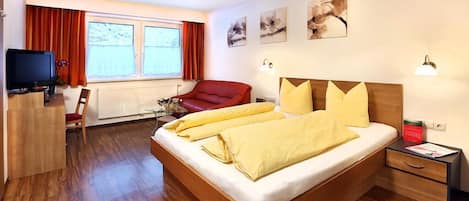 A modern hotel room with a wooden bed, red armchair, and a desk with a television.