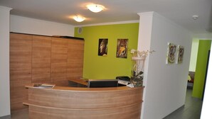 A reception desk with a wooden finish, a green wall with artwork, and a white pillar.