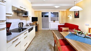 A compact kitchen with a microwave, stove, and coffee maker, a dining area with a table and chairs, and a red sofa.
