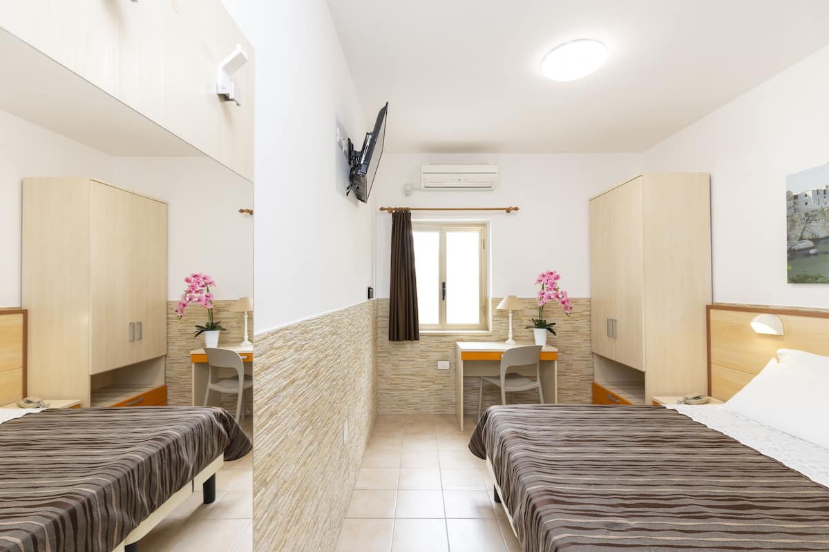 Una habitación de hotel con dos camas, un escritorio, una silla, un espejo y un equipo de aire acondicionado.