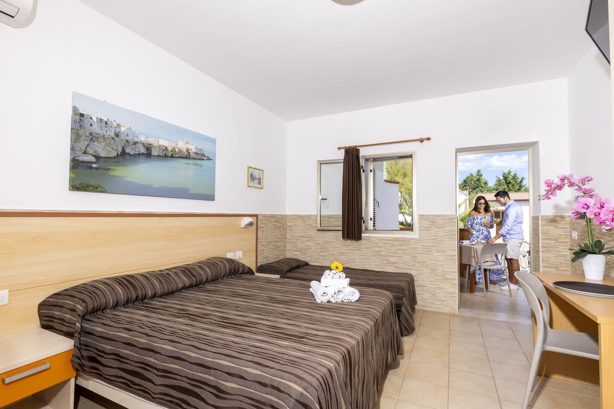 Habitación de hotel con dos camas, una zona de comedor, una ventana con vistas y un cuadro en la pared.