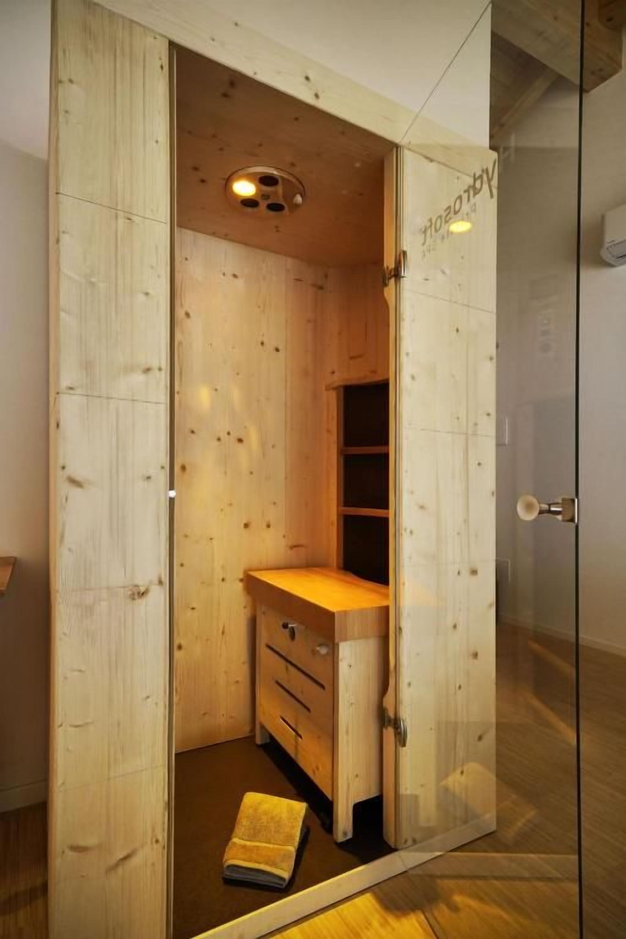 A wooden room with a built-in wardrobe, a small bench, and a door leading to another space.