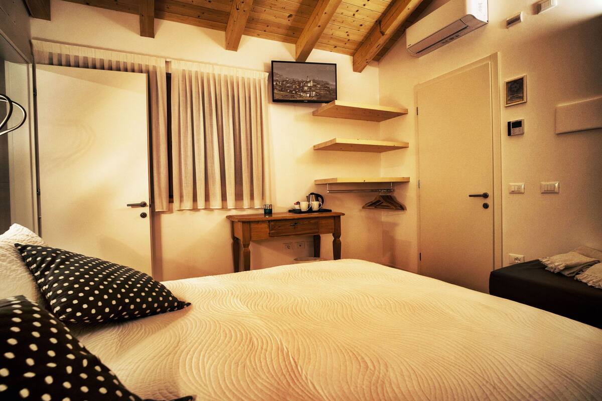 Une chambre à coucher avec un lit, une table de chevet, un téléviseur fixé au mur et une porte.
