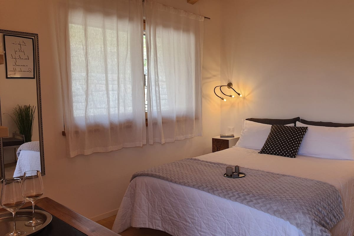 Une chambre à coucher bien rangée, avec un lit, des lampes de chevet, une table de chevet et une fenêtre ornée de rideaux légers.
