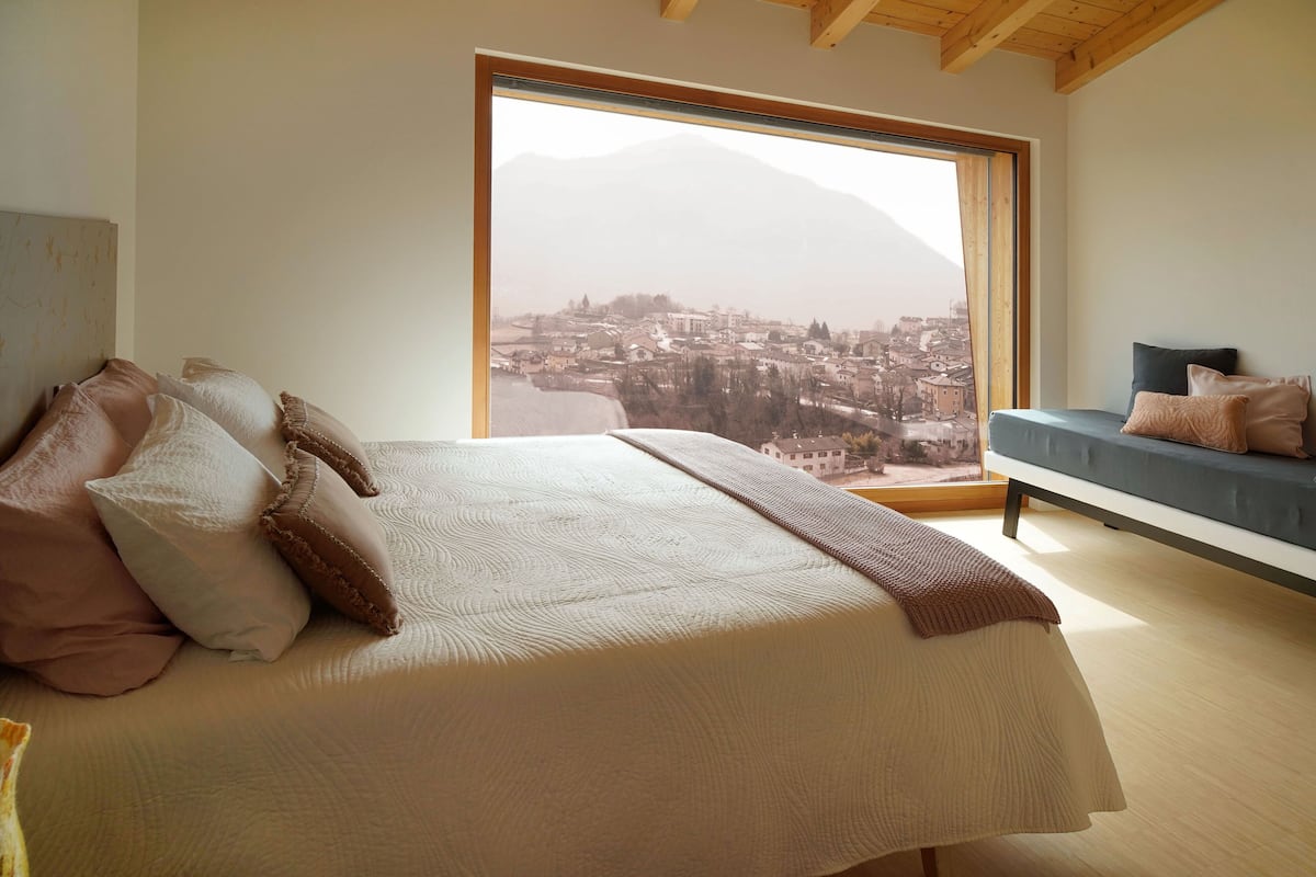 Une chambre avec un grand lit, une vue sur la ville par la fenêtre et un canapé avec des coussins.