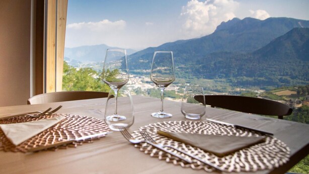 Mesa para dos con copas de vino y cubiertos, con vista a un paisaje montañoso.