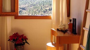 A cozy room with a wooden desk, a chair, a small table with candles, a TV mounted on the wall, and a window with a view of a forested landscape. - Hotel La Tinensa (La Pobla de Benifassa)