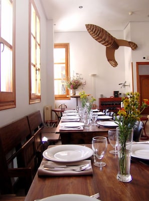 Un espace repas avec une longue table en bois dressée pour le repas, entourée de chaises en bois.