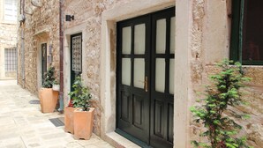 A narrow stone-paved street with a black door and a red mat with "WELCOME" on it. - Melek Accommodations (Dubrovnik)
