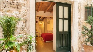 A rustic stone building with a wooden door, a bed with a red blanket, and a sign indicating it is apartment number 3. - Melek Accommodations (Dubrovnik)