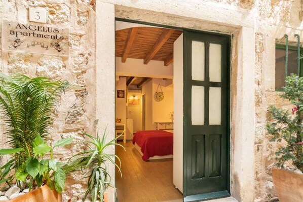 A rustic stone building with a wooden door, a bed with a red blanket, and a sign indicating it is apartment number 3.