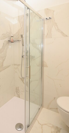 A modern bathroom with a glass-enclosed shower, marble walls, and a white toilet.