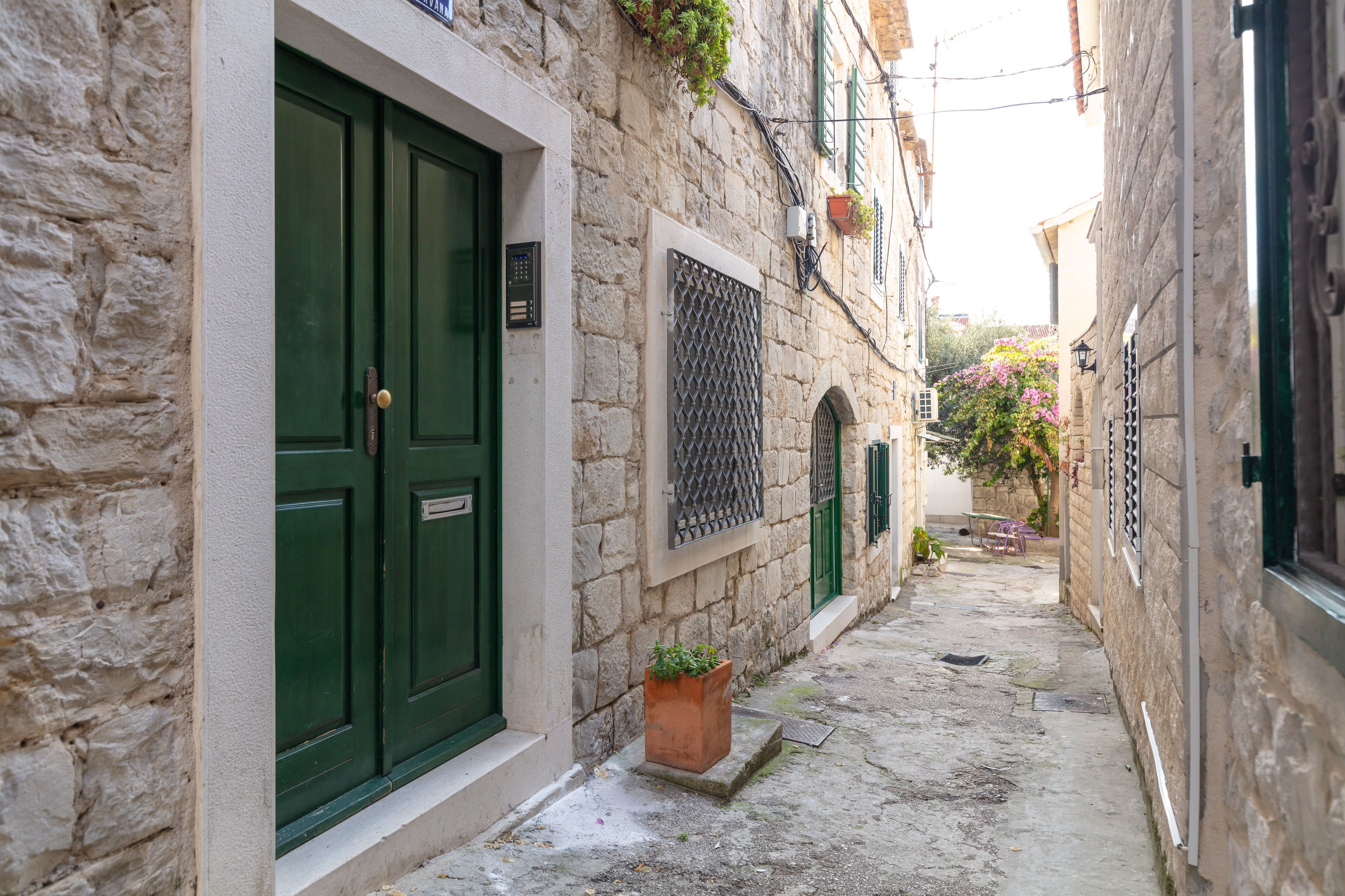 A narrow stone-paved alleyway with a green door and a window with a metal grille.