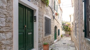 Un estrecho callejón empedrado con una puerta verde y una ventana con celosía metálica.