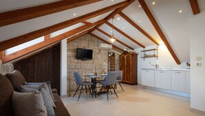 Un acogedor espacio tipo loft con zona de estar, una mesa de comedor y sillas, una pared de piedra y una cocina con armarios blancos.