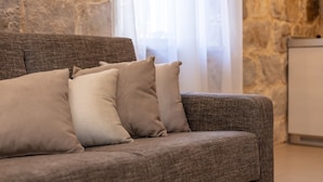 Un sofá gris con cojines beige en una habitación con paredes de piedra y un armario blanco.