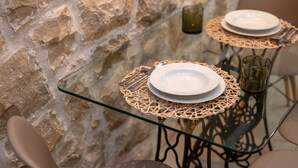 Un comedor con mesas de vidrio, individuales tejidas y un muro de piedra de fondo.