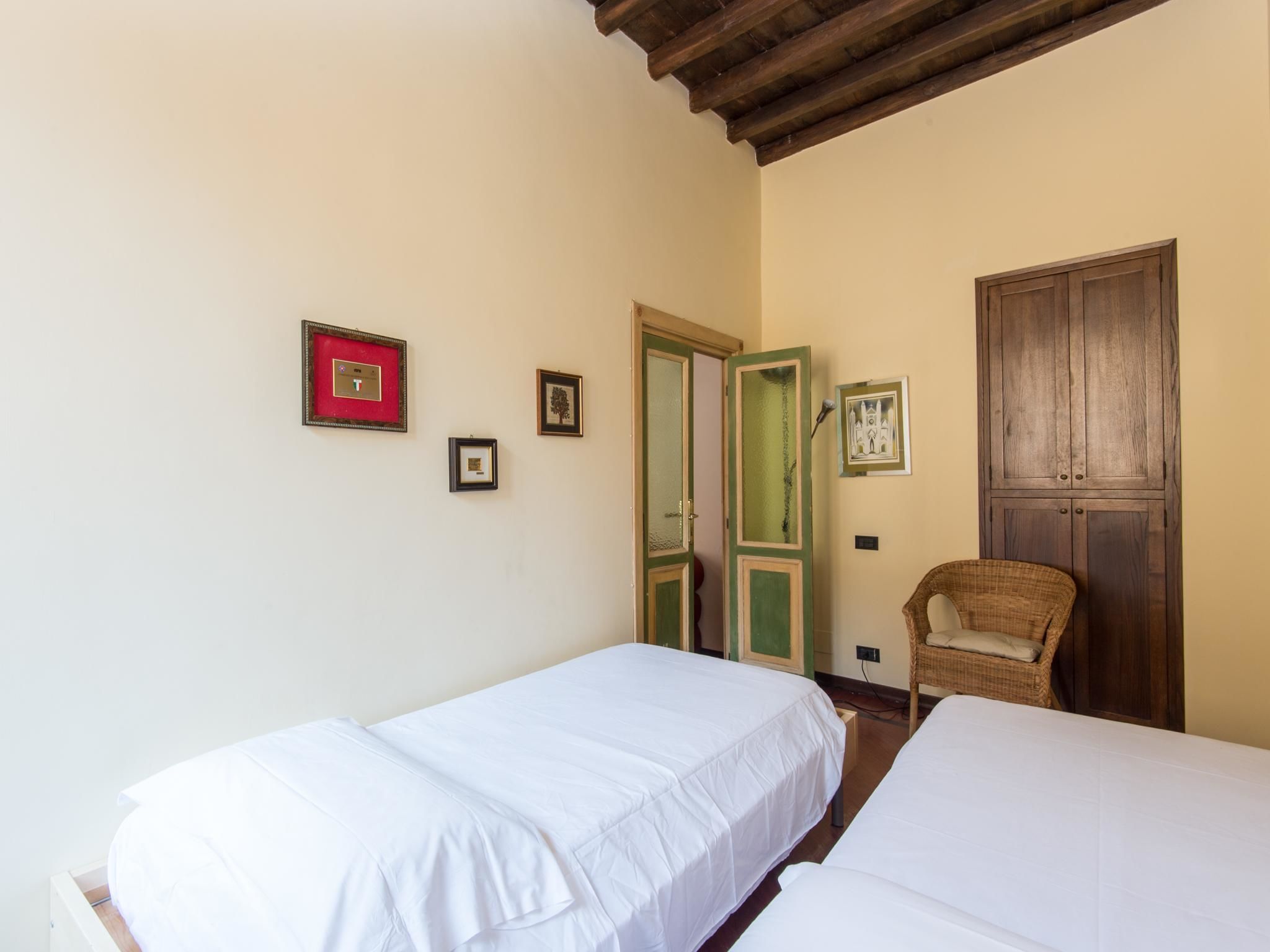 A room with two single beds, a wicker chair, and a wooden wardrobe.
