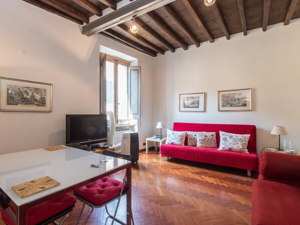 A room with a dining table, red sofa, and two framed pictures on the wall.