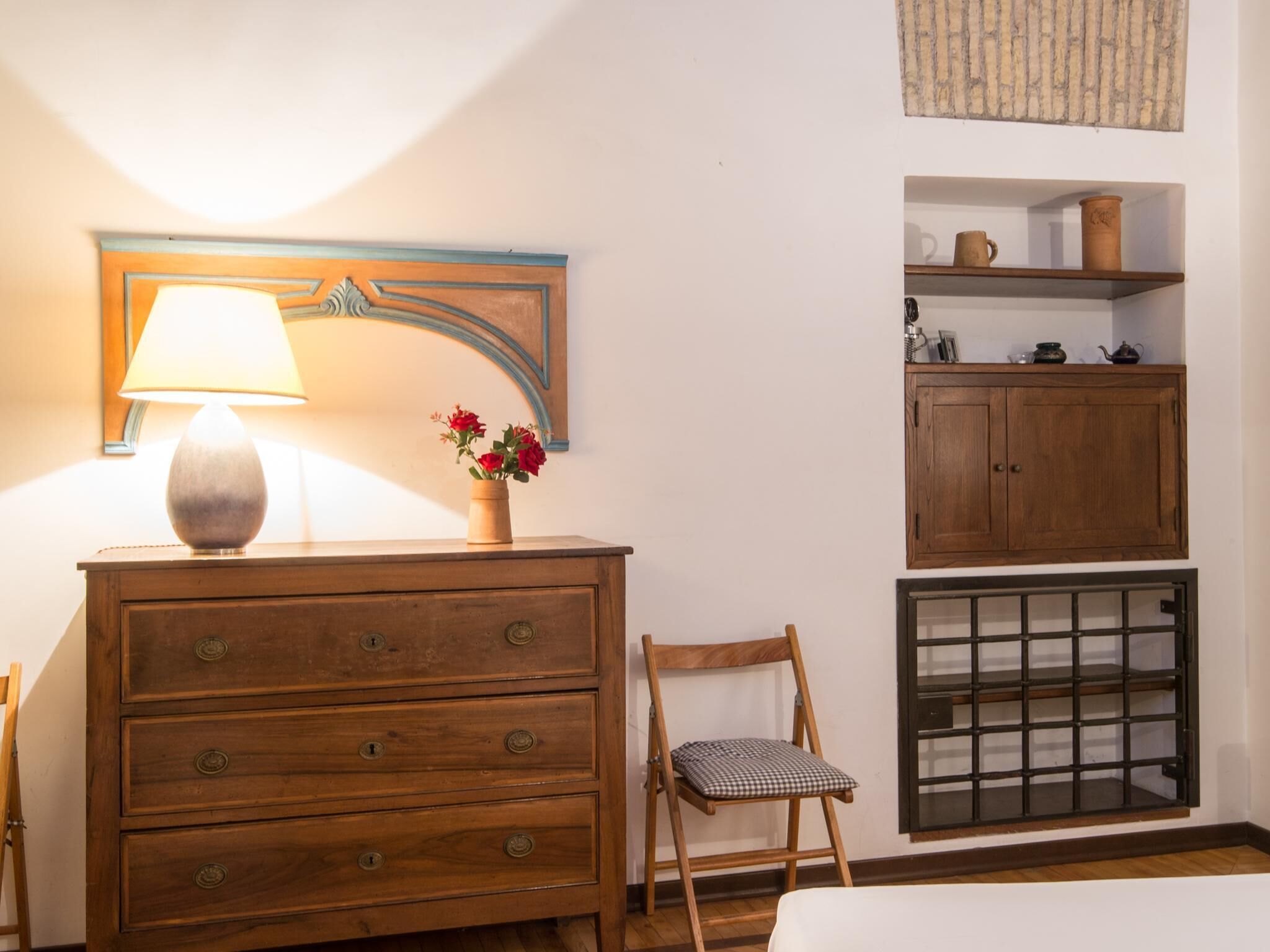 A wooden dresser with drawers, a lamp, and a vase with flowers.
