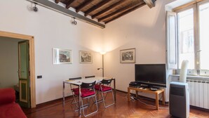 A room with a wooden floor, a dining table with chairs, a TV, and a radiator. - RSH Piazza Navona Charming Apartment 2 (Rome)