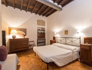 A bedroom with a wooden bed, a dresser, a chair, and a nightstand with a lamp.