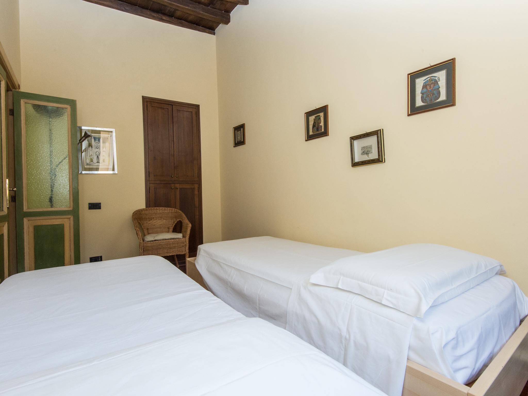 Una stanza con due letti singoli, un armadio in legno, una sedia in vimini e tre quadri appesi al muro.