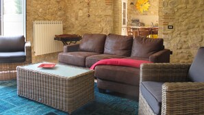 A cozy living room with a stone wall, a brown leather sofa, a wicker coffee table, and a dining area in the background.