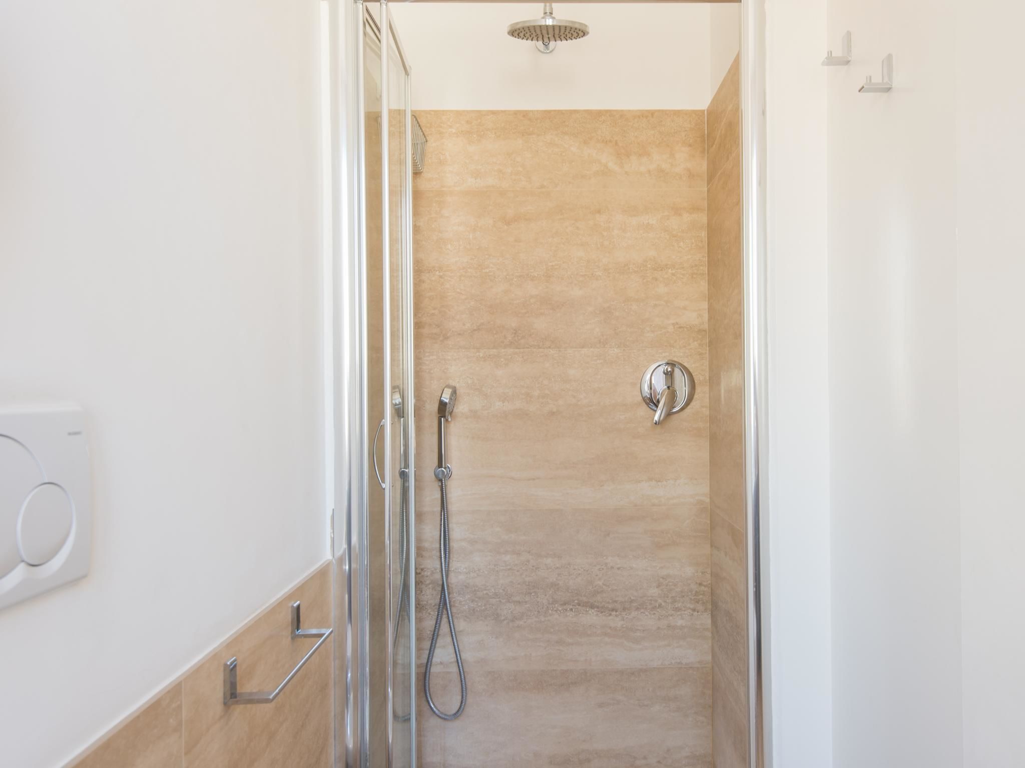A modern bathroom with a glass shower enclosure, beige tiled walls, and a chrome showerhead.