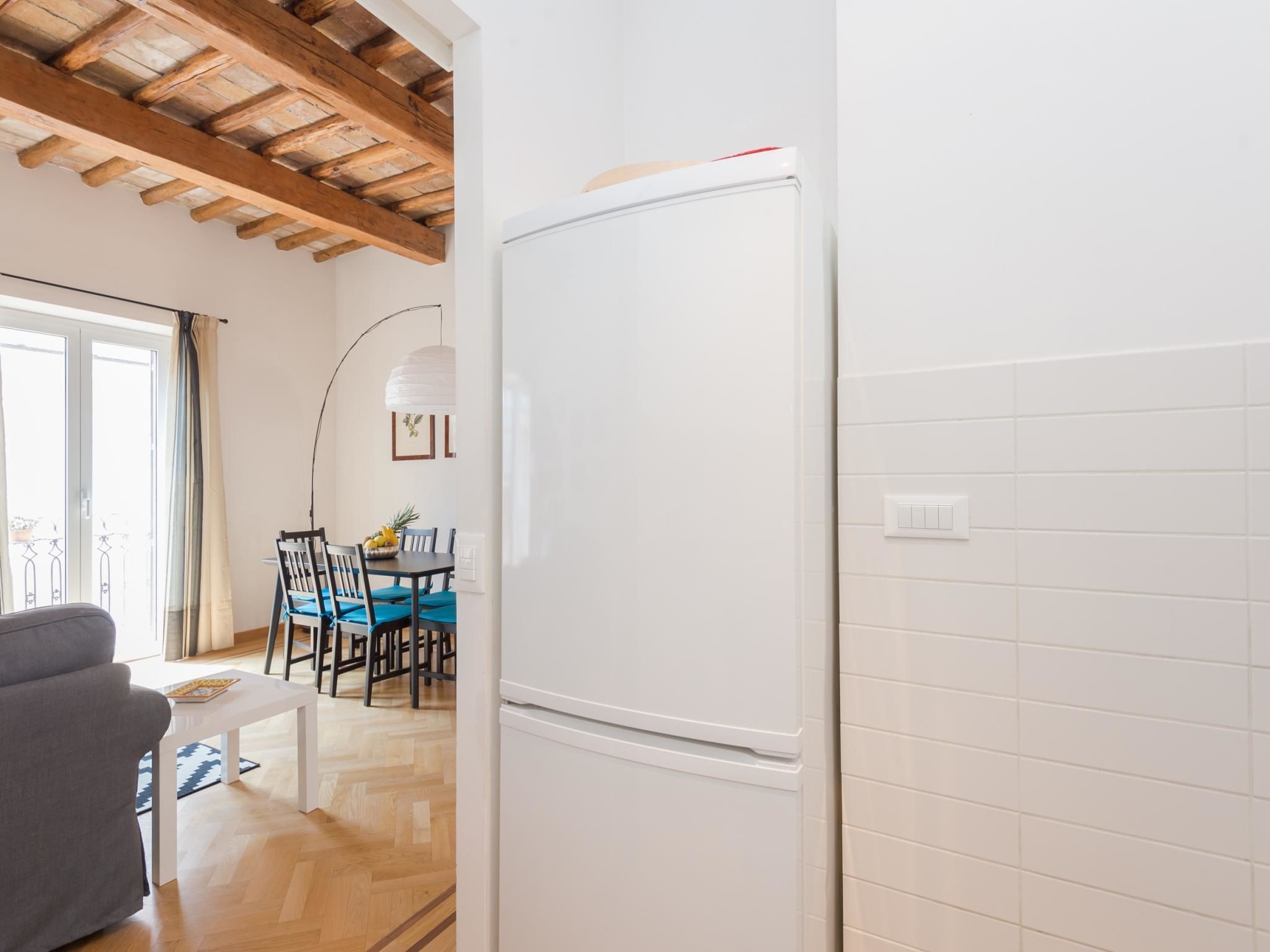 A modern kitchen with white tiled walls, a wooden ceiling, and a white refrigerator.
