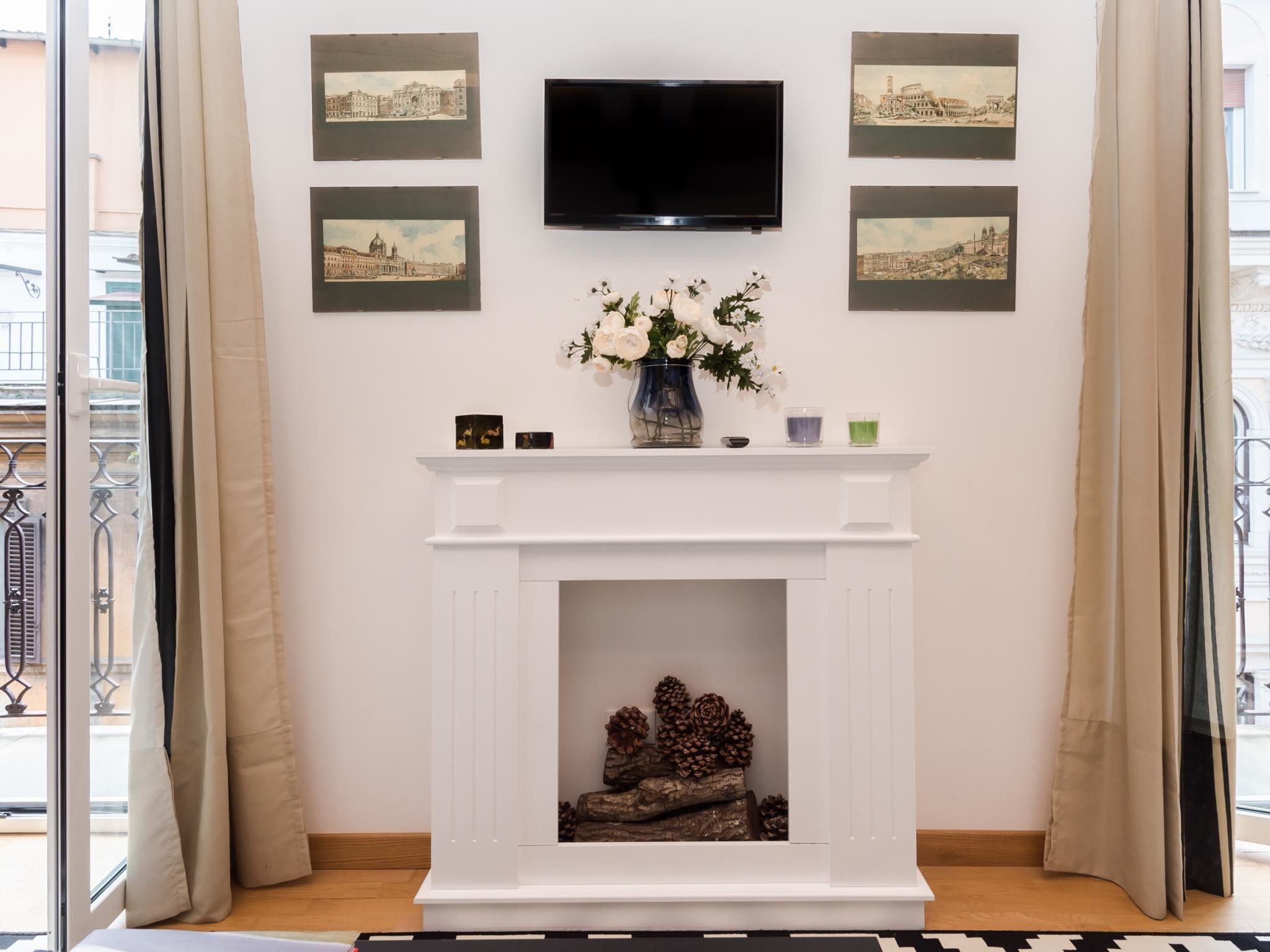 A living room with a white fireplace, a flat-screen TV mounted above it, and three framed cityscape pictures on the wall.