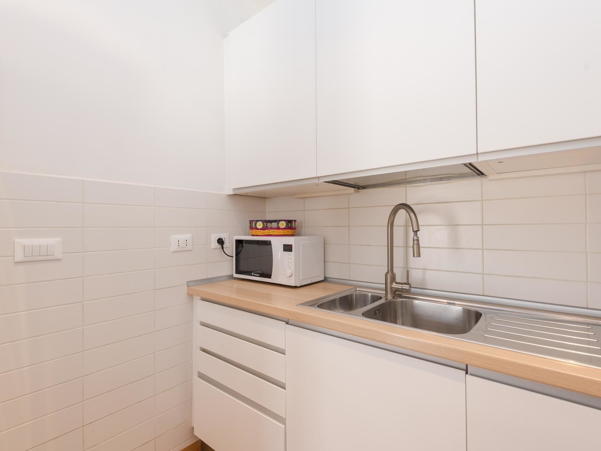 Une cuisine compacte avec des meubles blancs, un évier en acier inoxydable, un four à micro-ondes et un plan de travail en bois.