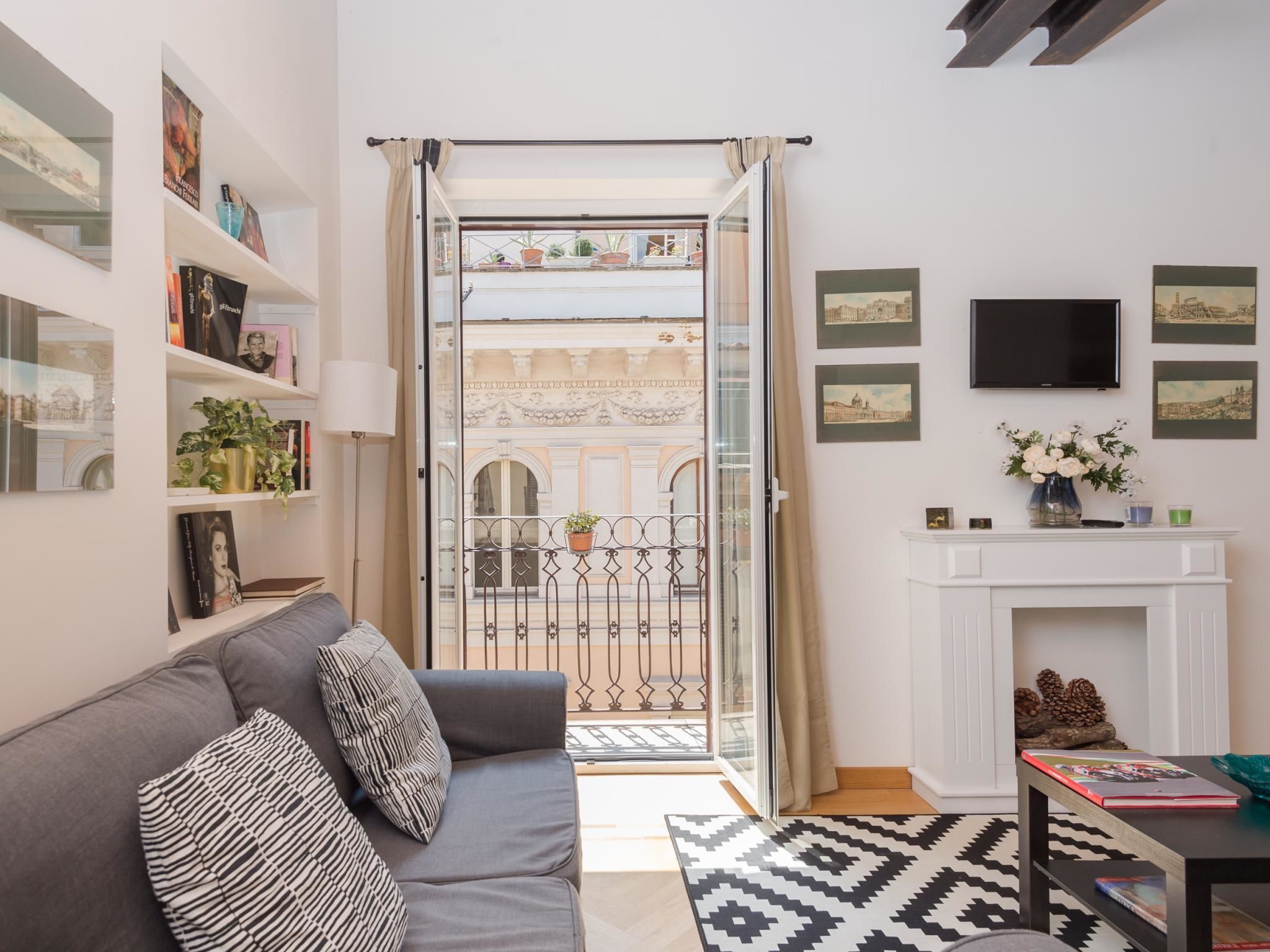 Un salon moderne avec un canapé gris, une cheminée et un balcon agrémenté d’une grille en fer forgé.