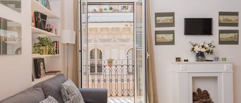 Un salon moderne avec un canapé gris, une cheminée et un balcon agrémenté d’une grille en fer forgé.