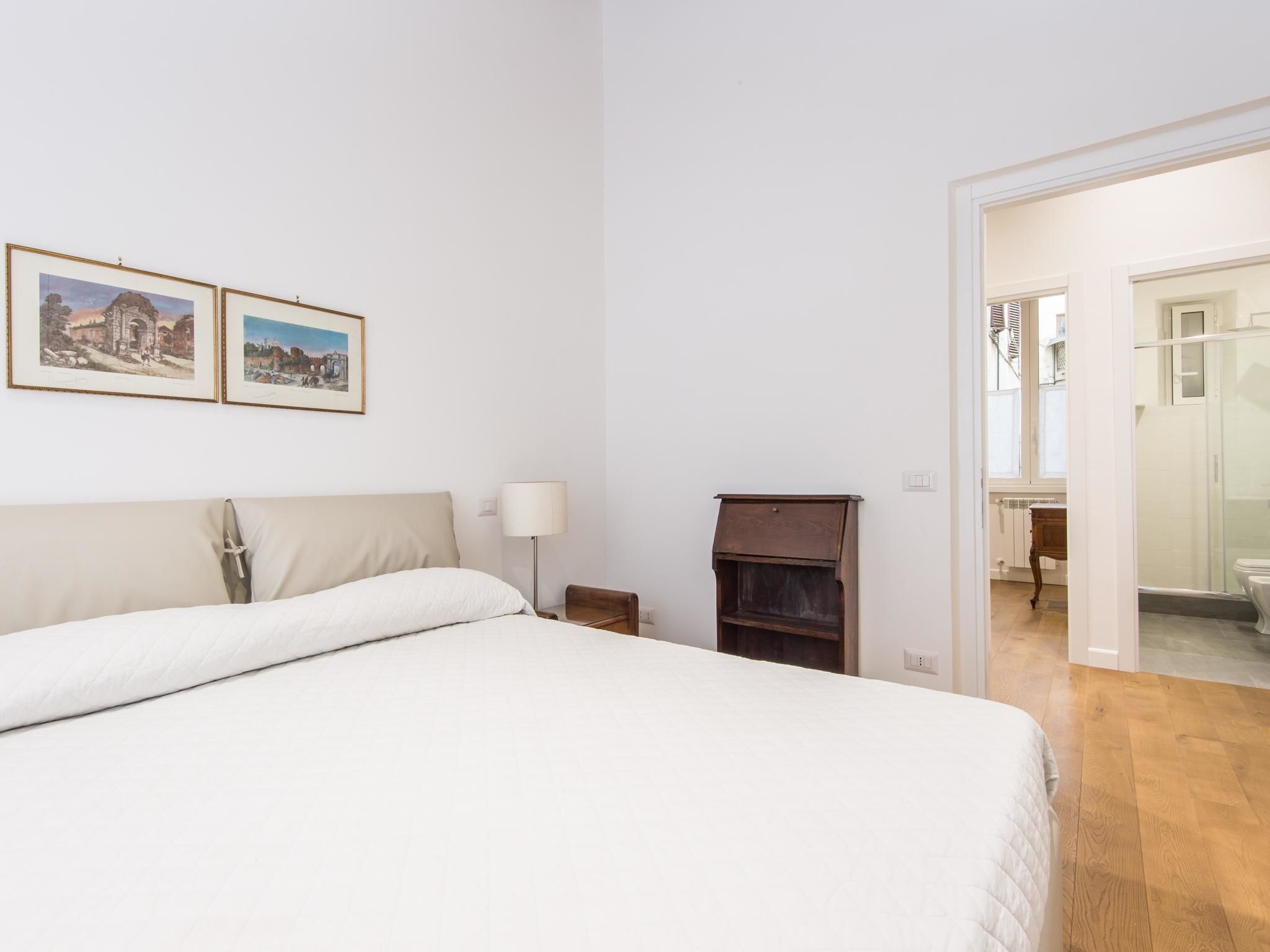 Un dormitorio con una cama, una mesita de noche, una lámpara, un armario de madera y dos cuadros en la pared.