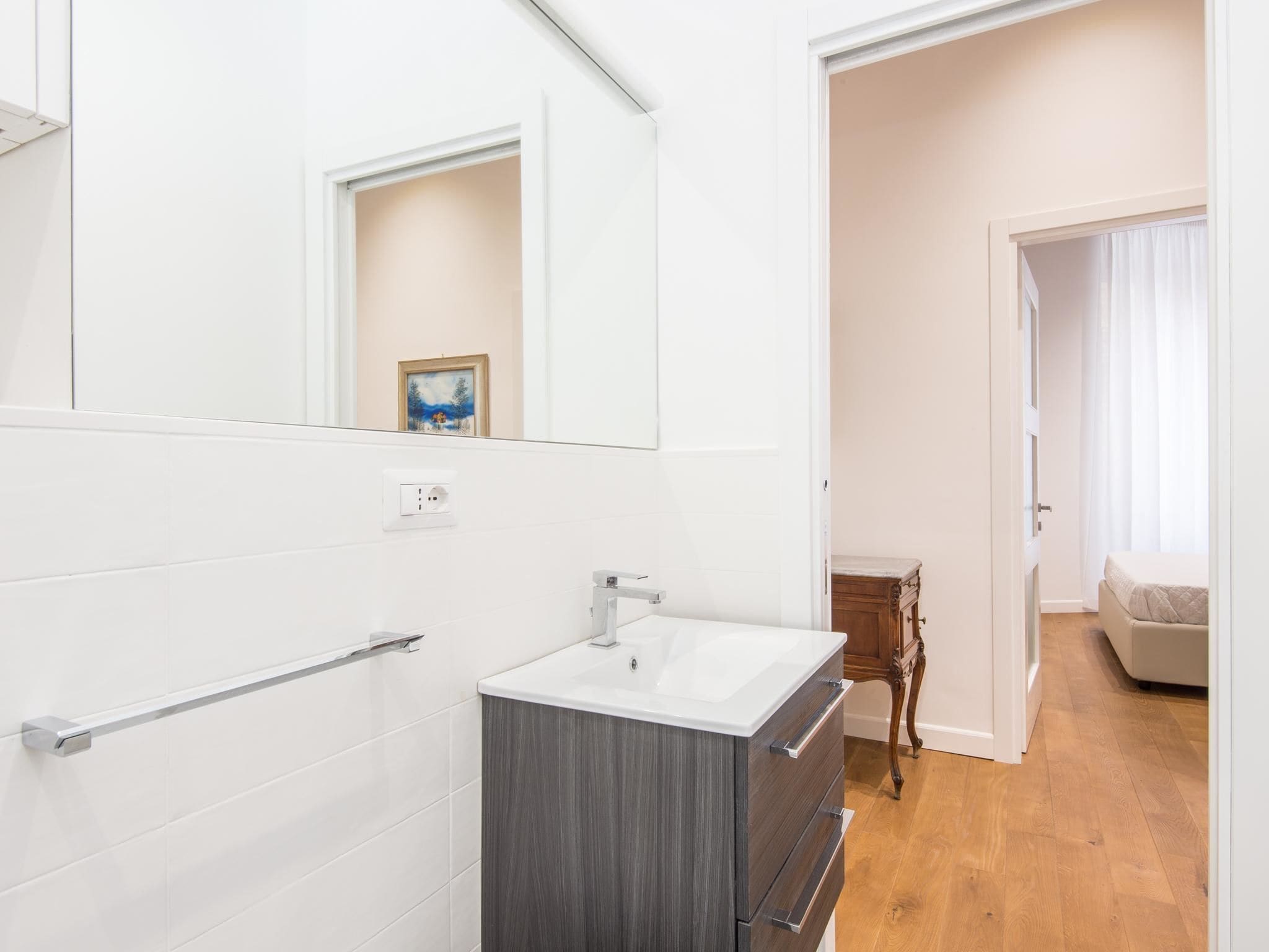 A modern bathroom with a white sink, a mirror, and a wooden cabinet.