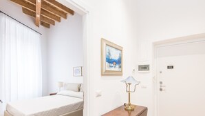 A bedroom with a bed, a bedside table with a lamp, a door, and a painting on the wall.