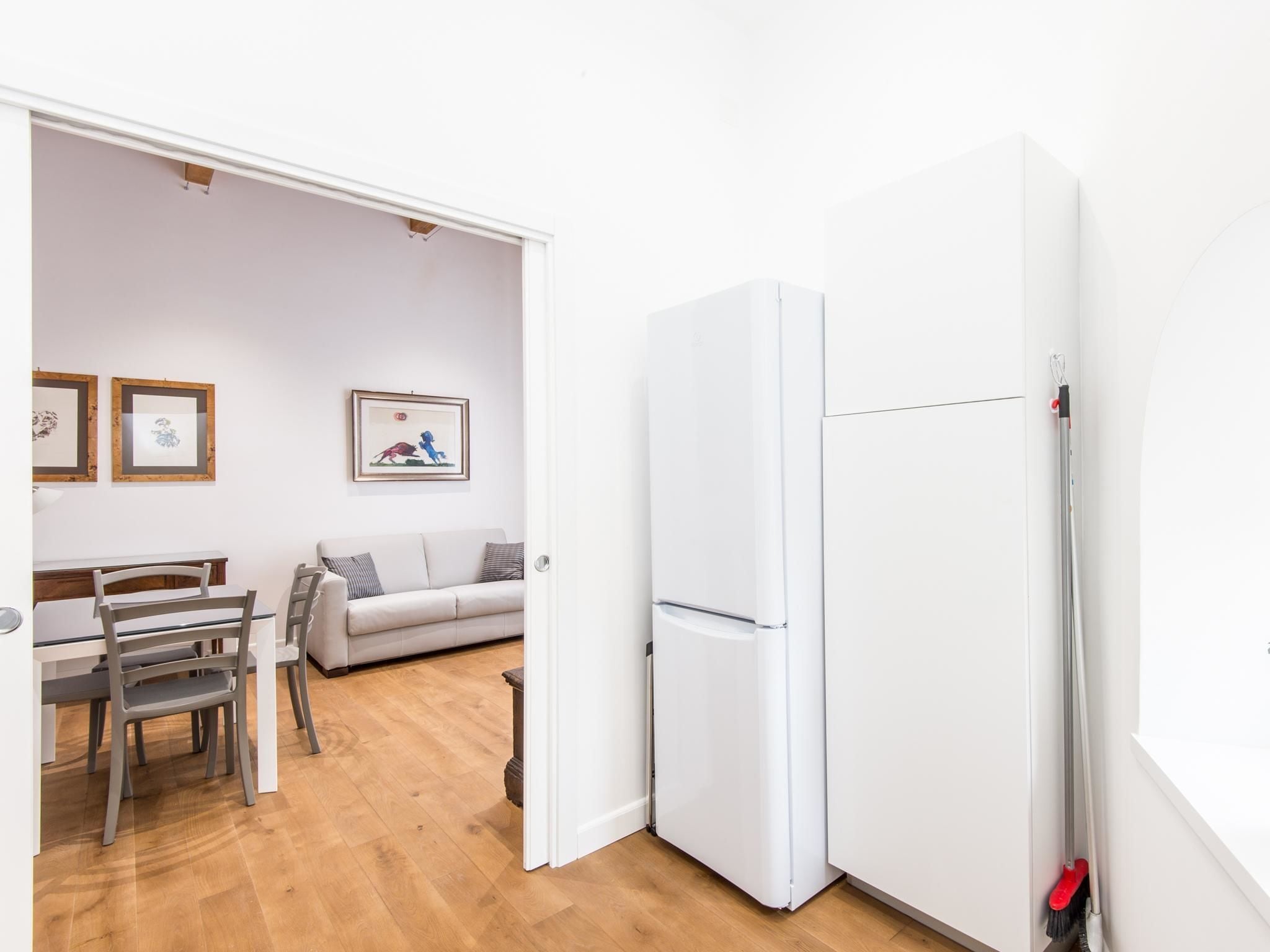 Eine moderne Küche mit weißen Geräten, ein Essbereich mit Tisch und Stühlen sowie ein Wohnzimmer mit Sofa und Wandbildern.