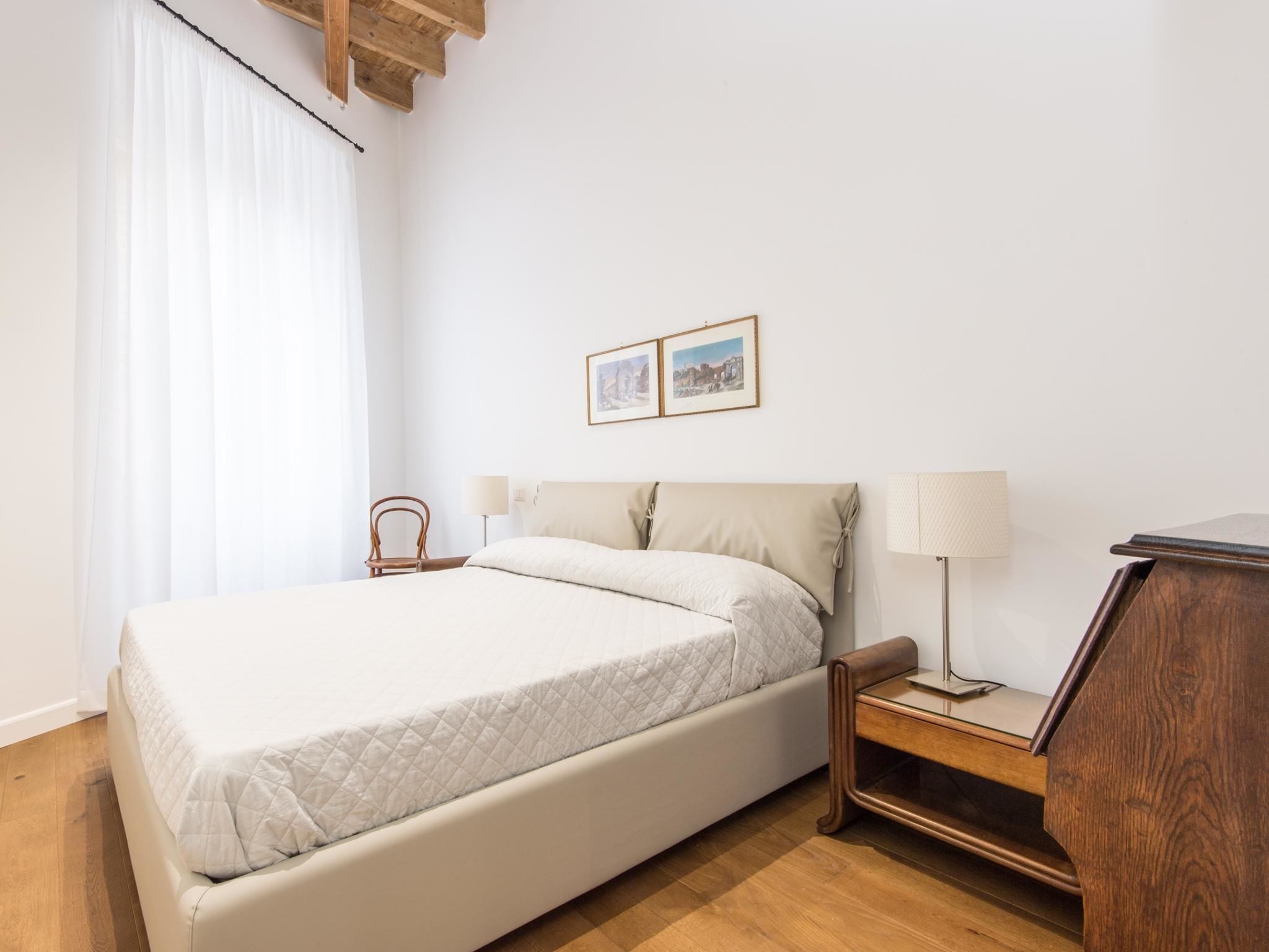Un dormitorio ordenado con cama, mesitas de noche, una silla y un escritorio.