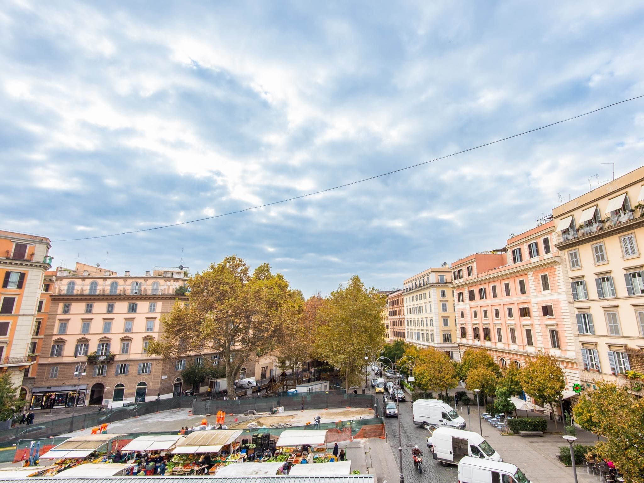 A bustling street scene with buildings, trees, and market stalls.
