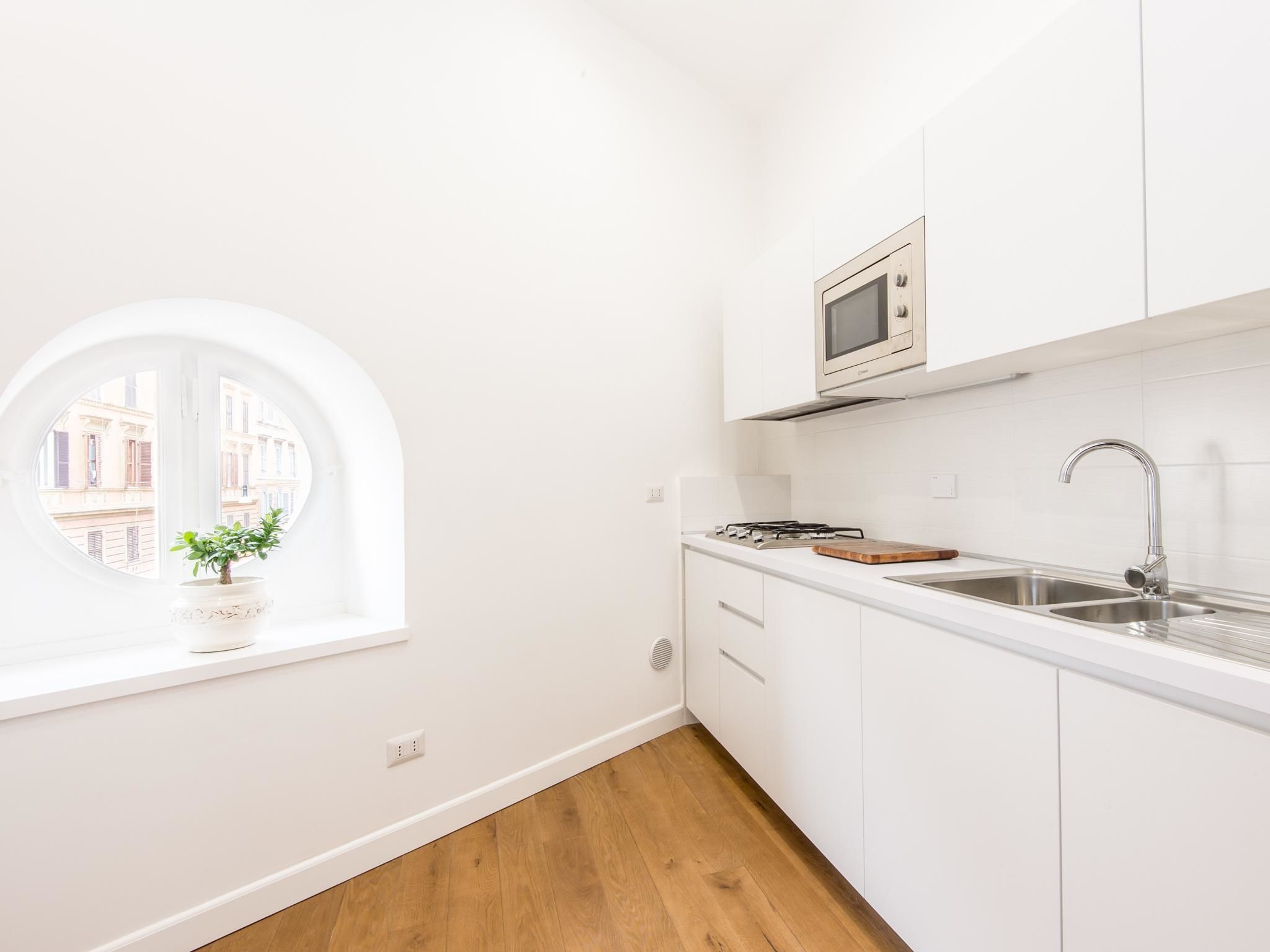 A modern kitchen with white cabinetry, a built-in microwave, a stainless steel sink, and a window with a view of buildings.