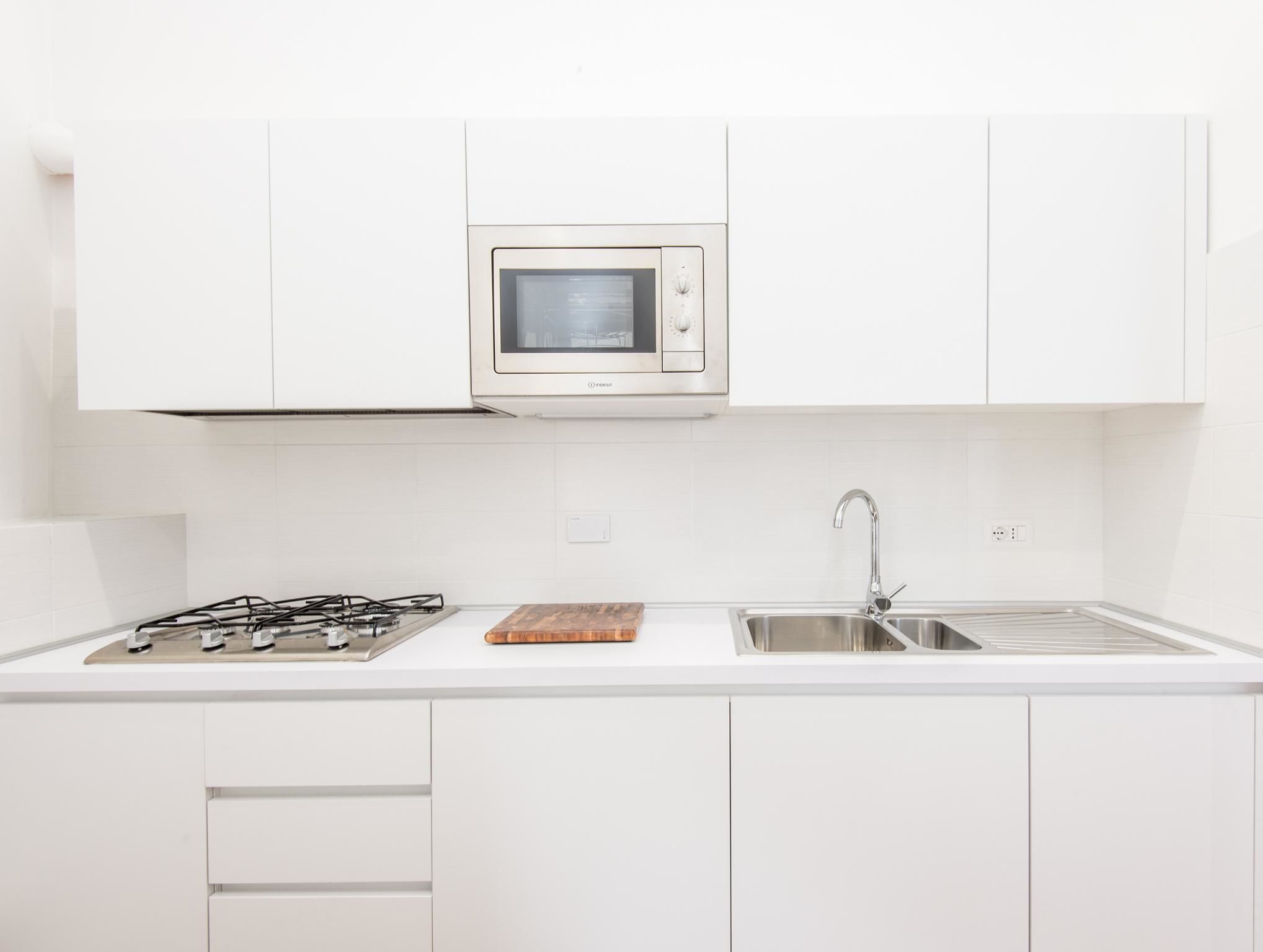 A modern kitchen with white cabinetry, a built-in microwave, a gas stove, and a stainless steel sink.